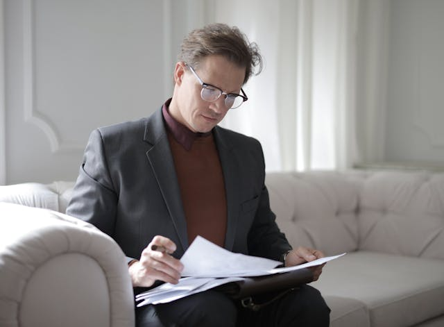 A-person-sitting-on-a-couch-reviewing-contracts A-person-sitting-on-a-couch-reviewing-contracts