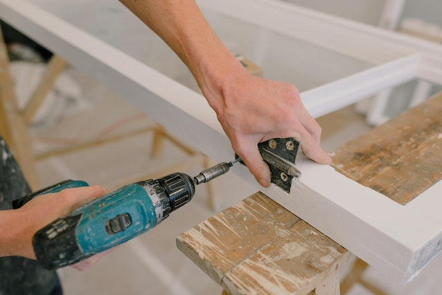 person-fixing-a-door-hinge-with-an-electric-drill person-fixing-a-door-hinge-with-an-electric-drill