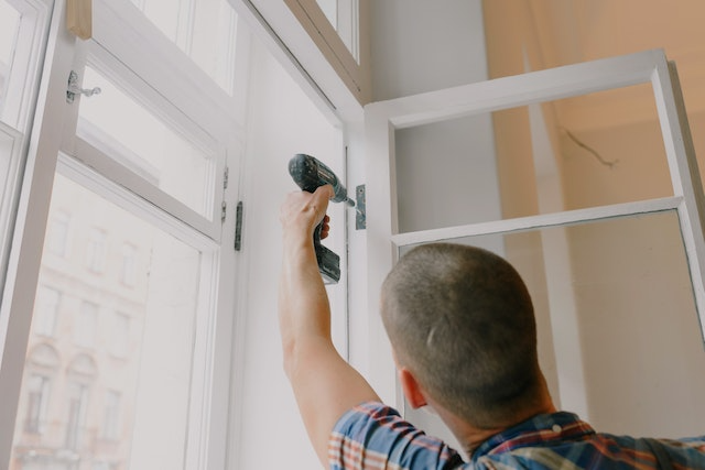 a-contractor-in-a-plaid-shirt-using-a-drill-to-fix-a-windows-hinge