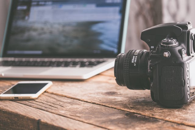 a-camera-cellphone-and-a-compter-on-a-wooden-table a-camera-cellphone-and-a-compter-on-a-wooden-table