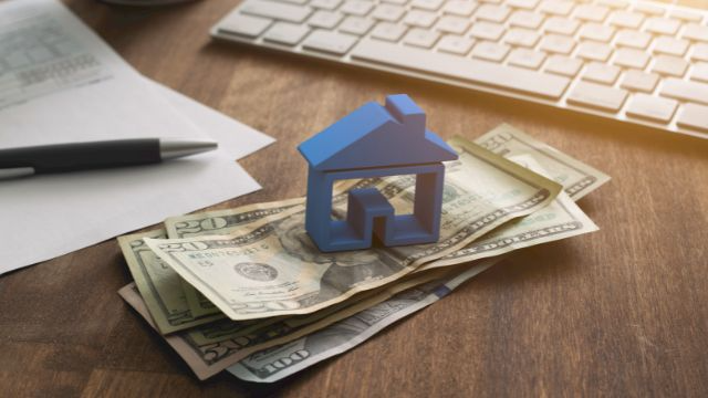 a-blue-home-figurine-resting-on-a-money-with-a-contract-in-the-background