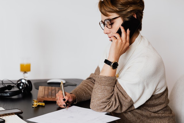 a landlord speaking the phone while taking notes at their desk